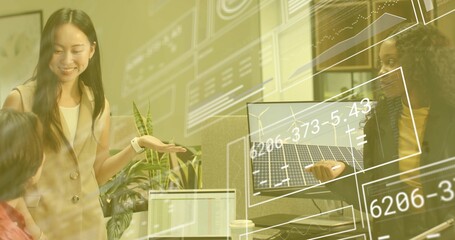 Asian female and colleagues gesturing at office desk, reviewing renewable energy data on monitors