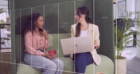 Discussing women wearing business attire in office lounge on green bench, with laptop and red mug
