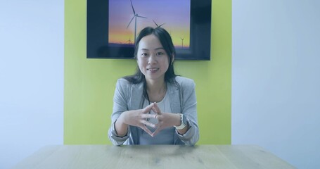 Sitting Chinese executive in blazer and smartwatch at meeting table, showing wind turbine display
