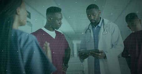Medical team members examining tablet in hospital corridor, with stethoscope burgundy blue scrubs