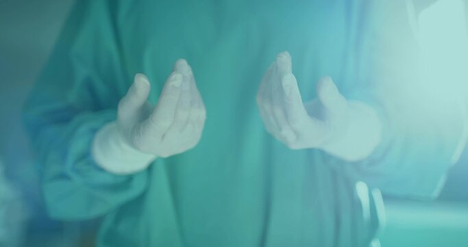 Holding surgeon holding sterile gloved hands at chest level in operating room with green scrubs