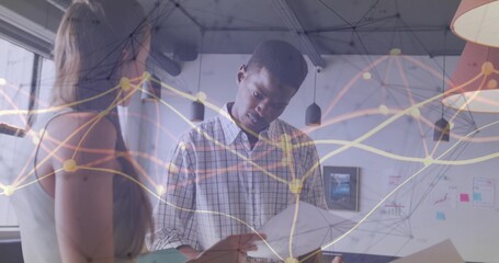 Reviewing papers coworkers wearing casual attire discussing data in office with network overlay