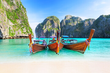 Beautiful white sand beach with three thai traditional wooden longtail boat and blue sky in Maya bay, Thailand. View of nice tropical beach with turquoise water in Maya bay near Phuket in Thailand.