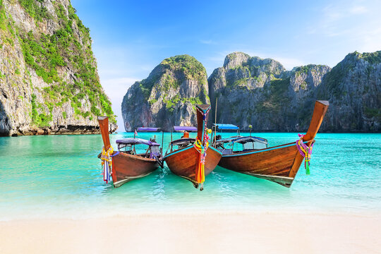Beautiful white sand beach with three thai traditional wooden longtail boat and blue sky in Maya bay, Thailand. View of nice tropical beach with turquoise water in Maya bay near Phuket in Thailand. - Powered by Adobe