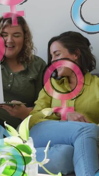 Animation of male and female symbols over lesbian couple using laptop