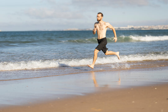 Barefoot man running on ocean beach exercising
