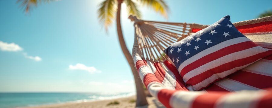 A hammock with an American flag pillow rests on a sunny beach. A palm tree waves gently overhead near the calm blue ocean. This scene evokes a sense of peaceful holiday leisure and national pride. - Powered by Adobe