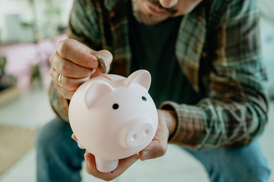 Mature man putting coin in piggy bank at home