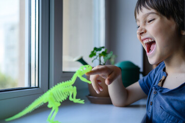 Child playing with dinosaur toy and smiling at home by the window