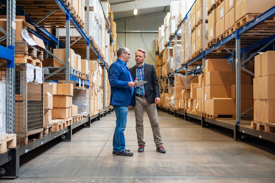 Businessmen discussing with tablet in warehouse aisle