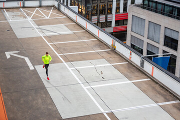 Athlete running on urban rooftop parking lot in bright yellow jacket