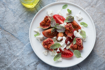 White plate with tomato, cottage cheese and figs salad, horizontal shot on a blue and beige stone background, above view