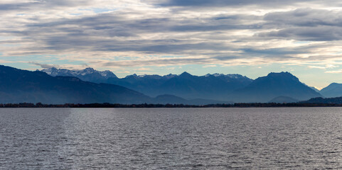 Dramatic panoramic view over the dark waters of Lake Constance (Bodensee) near Lindau, with the silhouette of the Swiss or Austrian Alps beneath a cloudy, moody sky