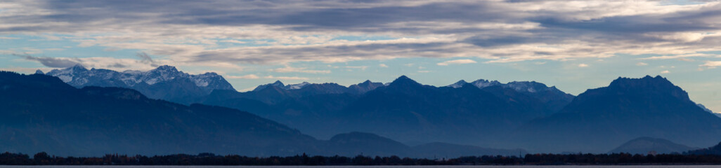 Dramatic panoramic view over the dark waters of Lake Constance (Bodensee) near Lindau, with the silhouette of the Swiss or Austrian Alps beneath a cloudy, moody sky