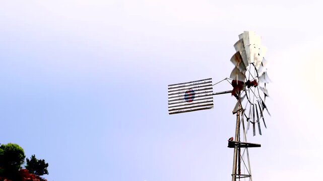 Old rusty windmill spinning in wind pumping up water on farm, slow motion