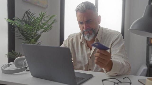 Man holding creditcard at building desk, hand on forehead for headache; online payment frustration debt.