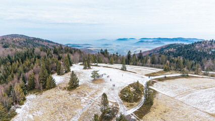 A tranquil winter panorama of Beskid Mały in southern Poland, where snowy meadows meet evergreen forests and rolling mountain hills under a serene, cloud-streaked sky.