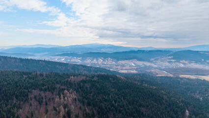 A tranquil winter panorama of Beskid Mały in southern Poland, where snowy meadows meet evergreen forests and rolling mountain hills under a serene, cloud-streaked sky.