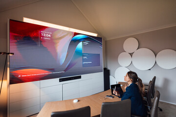 Businesswoman in modern office meeting room using big screen for online meeting