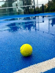 Blue paddle padel tennis court close up after rain. Tennis or paddle ball on the wet surface of the artificial grass court. Off season. Not playable.Matches are postponed or cancelled due to weather. 