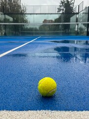 Blue paddle padel tennis court close up after rain. Tennis or paddle ball on the wet surface of the artificial grass court. Off season. Not playable.Matches are postponed or cancelled due to weather. 