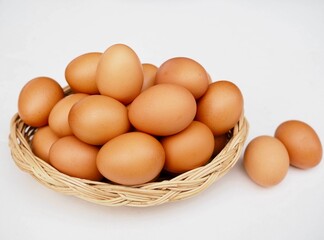 Several fresh chicken eggs are placed in a basket  on a white background.