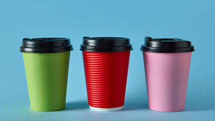 Three colorful takeaway coffee cups with black lids on blue background for packaging design. Concept of beverage product mockup, branding, and cafe industry marketing visuals.