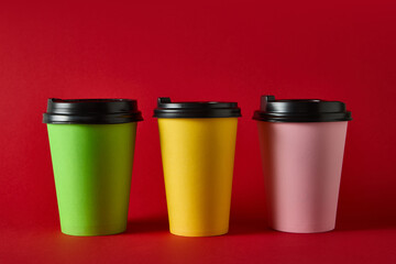 Three colorful takeaway coffee cups with black lids on blue background for packaging mockup. Concept of beverage packaging, cafe marketing, product ads for catering