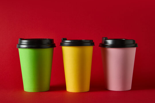 Three colorful takeaway coffee cups with black lids on blue background for packaging mockup. Concept of beverage packaging, cafe marketing, product ads for catering