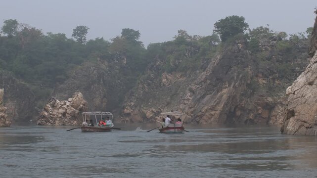 scenic river gorge with boats rowing between towering marble rock cliffs and deep calm flowing water surrounded by nature, marble rocks, jabalpur, india