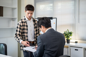 Asian man explaining document to businessman boss during work presentation in company office.