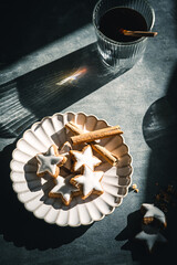 Gebackene Zimtsterne auf einem Teller und ein Glas Kaffee im harten Licht. Moody, grauer Tisch, Draufsicht.