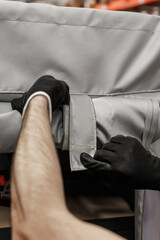 Obraz premium Close-up of gloved hands fastening a heavy-duty Velcro strap on a gray industrial textile cover, set in a warehouse environment