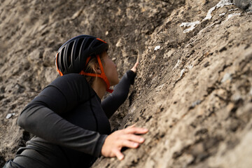 Woman rock climber in helmet ascending cliff during outdoor climbing session on natural terrain during daytime, view from bottom to top, portrait
