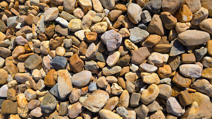 texture of a natural assortment of pebbles and river stones in warm earth tones, ideal for landscaping, garden borders, pathways, or decorative rock surfaces
