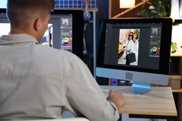 Professional retoucher editing photo on computer at table in office, back view