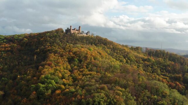 Aerial view of Burgruine Auerbach perched atop a hill with colorful autumn trees, under a partly cloudy sky, Bensheim, Hessen, Germany.