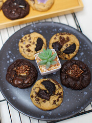 Close up freshly baked homemade chocolate soft cookies mixed toppings biscuits wafer chocolate chips on black ceramic plate decorate with little tree dessert snack bakery yummy delicious tasty concept