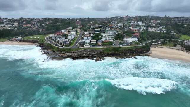 Aerial view of the rugged Bronte Beach coastline where turquoise waves crash against the rocks near the sandy shore, Sydney, New South Wales, Australia.