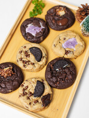 Close up freshly baked homemade chocolate soft cookies mixed toppings biscuits wafer chocolate chips on wooden board, decorate with small christmas tree, pine cones, Merry christmas and Happy new year