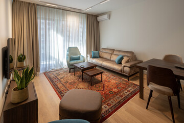 Cozy living room interior with beige sofa, blue armchair, and oriental carpet