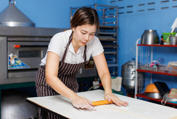 Asian beautiful woman baker wearing striped apron preparing knead dough by hand in bakery kitchen professional female making pastry bread with care homemade baking craftsmanship small business concept