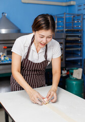 Asian beautiful woman baker wearing striped apron preparing knead dough by hand in bakery kitchen professional female making pastry bread with care homemade baking craftsmanship small business concept