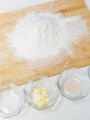 Top view, picture frame of baking pastry or cake ingredients for bread bakery, flour, yeast, water, butter on wooden cutting board on a white table, homemade preparation process making cooking concept