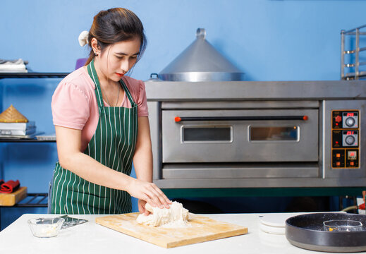 Asian beautiful young woman bakers wearing striped aprons knead dough on wooden cutting board mixing flour baking process different ingredients making homemade bread pastry in bakery kitchen concept.