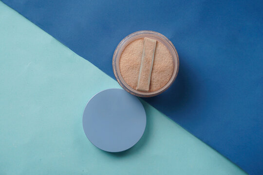 A Wardah powder with its lid opened is placed on a mix of dark blue and light blue background, creating a clean and elegant scene