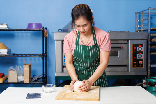 Asian beautiful young woman bakers wearing striped aprons knead dough on wooden cutting board mixing flour baking process different ingredients making homemade bread pastry in bakery kitchen concept.