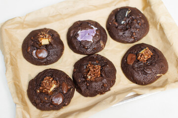 Close up freshly baked homemade dark chocolate soft cookies mixed toppings biscuits wafer marshmallow chocolate chips on baking tray parchment paper sheet, Dessert snack bakery yummy delicious tasty.