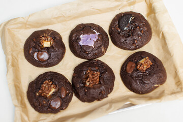 Close up freshly baked homemade dark chocolate soft cookies mixed toppings biscuits wafer marshmallow chocolate chips on baking tray parchment paper sheet, Dessert snack bakery yummy delicious tasty.