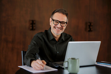 Businessman working from home with laptop and notes, smiling